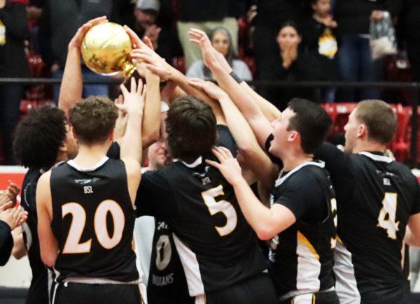 Go for gold--Senior forward Brett Boyles reaches over his teammates to touch the bi-district trophy after the Indian win on Feb. 17. Boyles had ten points in the win.